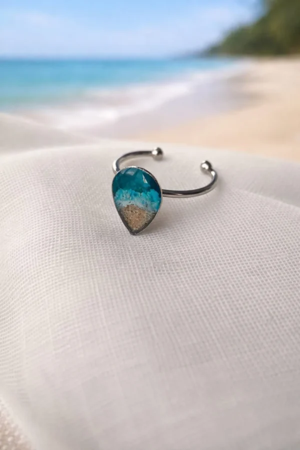 Anillo abierto con gota de resina y arena sobre tela de lino