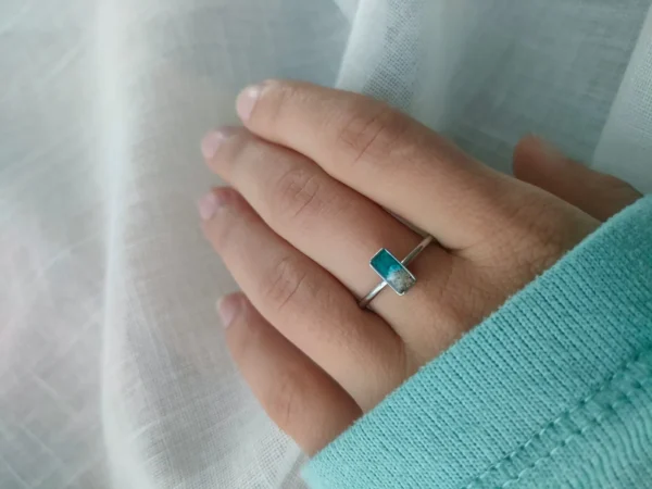 Anillo con piedra rectangular de resina turquesa en una mano